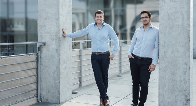 Die zwei brighter AI Gründer stehen zwischen zwei grauen Säulen